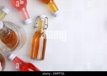 Savoureux kombucha dans des bouteilles en verre sur une table carrelée blanche, pose à plat. Espace pour le texte Banque D'Images