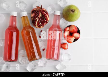 Savoureux kombucha dans des bouteilles en verre, fruits frais et glace sur table blanche, plat. Espace pour le texte Banque D'Images