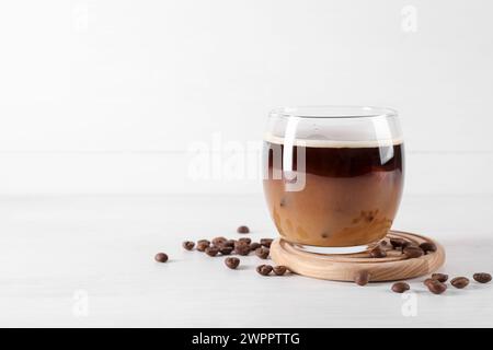 Café glacé rafraîchissant avec du lait en verre et des haricots sur une table en bois blanc, espace pour le texte Banque D'Images