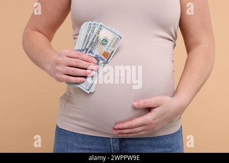 Mère porteuse. Femme enceinte avec des billets de banque en dollars sur fond beige, gros plan Banque D'Images