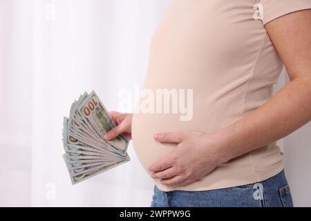 Mère porteuse. Femme enceinte avec des billets de banque en dollars à l'intérieur, gros plan Banque D'Images