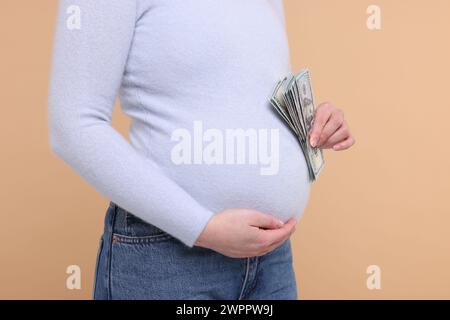 Mère porteuse. Femme enceinte avec des billets de banque en dollars sur fond beige, gros plan Banque D'Images