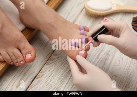 Pédicuriste professionnel peignant les ongles des orteils du client avec du vernis dans le salon de beauté, gros plan Banque D'Images