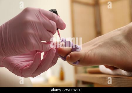 Pédicuriste professionnel peignant les ongles des orteils du client avec du vernis dans le salon de beauté, gros plan Banque D'Images