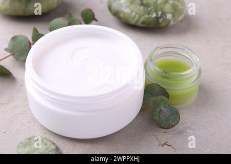 Pots de crème et feuilles vertes sur table texturée légère. Produits de soins corporels Banque D'Images