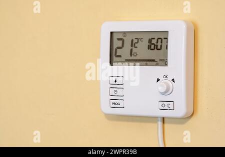 Unité de thermostat numérique programmable pour maison intelligente moderne montée sur un mur jaune à l'intérieur d'une maison, montrant la température ambiante actuelle et la température réglée Banque D'Images