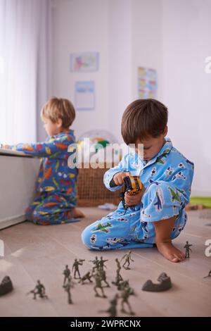 Garçons, jouets et jeunes enfants en pyjama jouant pour le plaisir avec des figurines d'action, voiture ou jeux. Frères, développement de l'enfant et liens entre jeunes enfants Banque D'Images