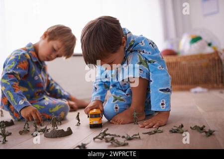 Garçons, jouant et enfants en pyjama avec des jouets pour s'amuser avec des figurines d'action, voiture ou jeux. Frères, développement de l'enfant et jeunes enfants qui s'unissent Banque D'Images