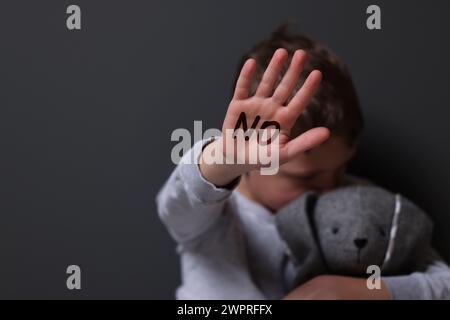 Maltraitance des enfants. Garçon avec lapin jouet faisant un geste d'arrêt près du mur gris, mise au point sélective. Non écrit sur sa main Banque D'Images