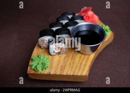 Assortiment de sushis avec une variété de rouleaux et de sashimis magnifiquement disposés sur une assiette en bois, accompagnés de baguettes et d'un côté de soja salé Banque D'Images