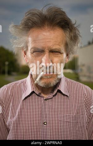 Homme âgé fumant des cigarettes dans le parc de la ville dernièrement le jour Banque D'Images