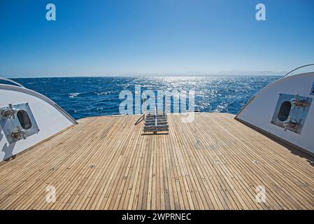 Échelles en acier métallique sur le pont arrière en bois de teck d'un grand yacht à moteur de luxe naviguant sur un océan tropical à coucher de soleil Banque D'Images