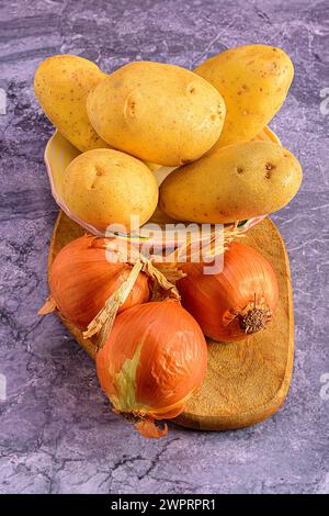 Oignons et pommes de terre sur planche à découper en bois sur comptoir en marbre, gros plan Banque D'Images