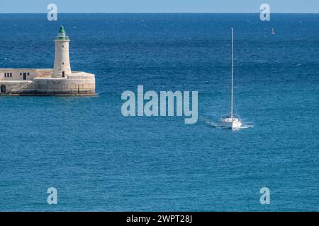 Un bateau pénètre dans le Grand Port de la Valette avec les équipés Phare de brise-lames Elmo en arrière-plan Banque D'Images