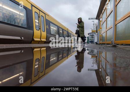 Passager embarquant dans un train Merseyrail Stadler classe 777 à la gare de Bebington reflété dans une flaque sur le quai de la gare Banque D'Images