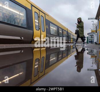 Passager embarquant dans un train Merseyrail Stadler classe 777 à la gare de Bebington reflété dans une flaque sur le quai de la gare Banque D'Images