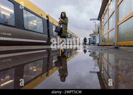 Passager embarquant dans un train Merseyrail Stadler classe 777 à la gare de Bebington reflété dans une flaque sur le quai de la gare Banque D'Images