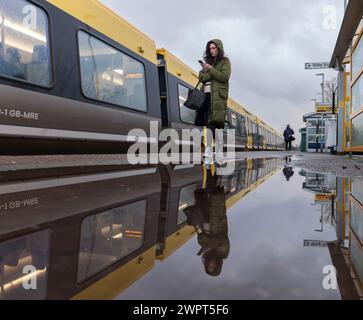 Passager embarquant dans un train Merseyrail Stadler classe 777 à la gare de Bebington reflété dans une flaque sur le quai de la gare Banque D'Images