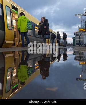 Les passagers qui partent et montent dans un train Merserail à la gare de Bebington se reflètent dans une flaque d'eau Banque D'Images
