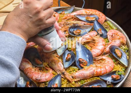 Gros plan d'une main assaisonnant la paella traditionnelle aux fruits de mer avec des couleurs riches, cuisine espagnole typique, Majorque, Îles Baléares, Espagne Banque D'Images