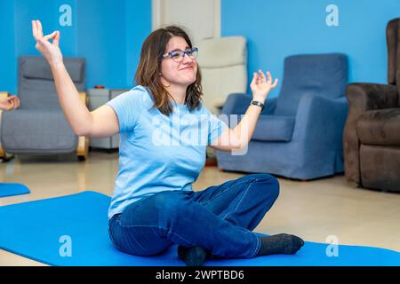 Femme avec des besoins spéciaux appréciant pendant le cours de yoga assis en position lotus et les bras levés Banque D'Images