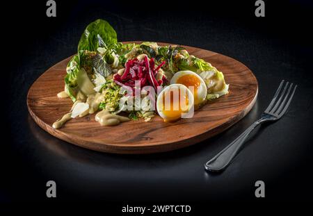 Salade sur assiette en bois avec oeuf dur mou Banque D'Images