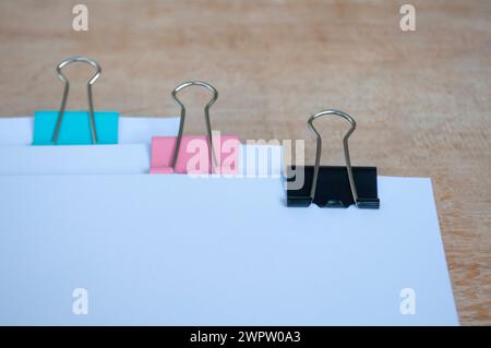 Vue latérale de papiers de document vierges avec trombones pastel sur table en bois. Concept de documentation. Banque D'Images