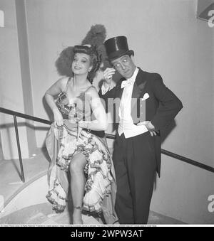 Au théâtre en 1950. Un homme et une femme vêtus de leurs vêtements de scène avant un spectacle dans les coulisses. Vêtu d'un manteau et d'un chapeau haut de gamme, il se tient debout et regarde de près sa collègue à travers un monocle alors qu'elle soulève sa longue jupe pour révéler ses jambes bas. 1950. Kristoffersson ref AZ12-8 Banque D'Images