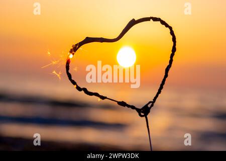 Étincelant en forme de coeur brûlant sur fond de mer et soleil levant à l'aube. Feu du Bengale en forme de coeur scintillant à l'aube du lever du soleil et au coucher du soleil sur la mer. Amour engouement Saint-Valentin Banque D'Images