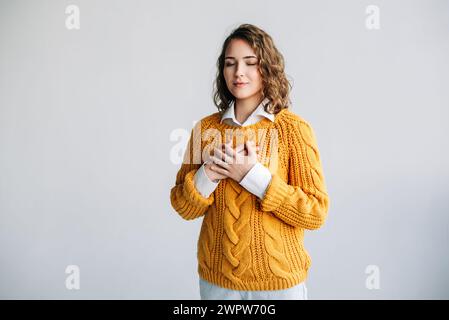 Femme reconnaissante : mains sur la poitrine, exprimant le bonheur, équilibre mental - reconnaissance, gentillesse, amour - Portrait isolé sur fond blanc - Banque D'Images