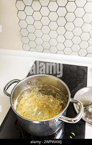 Une casserole en acier inoxydable remplie d'eau bouillante pour cuire les pâtes al dente sur une plaque vitrocéramique à deux brûleurs Banque D'Images