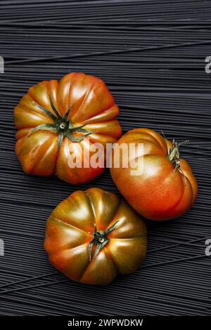 Un trio de succulentes tomates Raf mûres sur un monticule de pâtes noires Banque D'Images