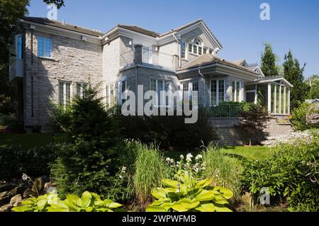 Frontière avec Hosta et Miscanthus - plantes d'herbe ornementale dans la cour arrière paysagée et vue arrière de la brique grise de deux étages et maison en pierre en été. Banque D'Images