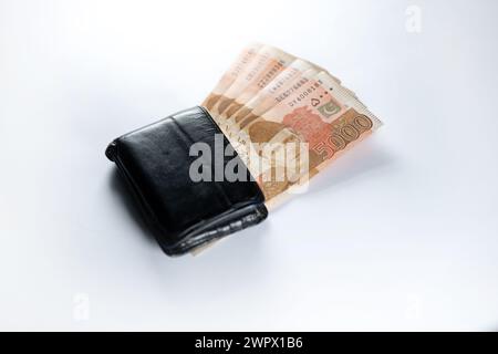 Cinq mille billets de banque de 5000 roupies alignés avec un portefeuille en cuir noir. Pakistan State Bank billets de monnaie officielle 2024 isolé sur fond blanc. Banque D'Images