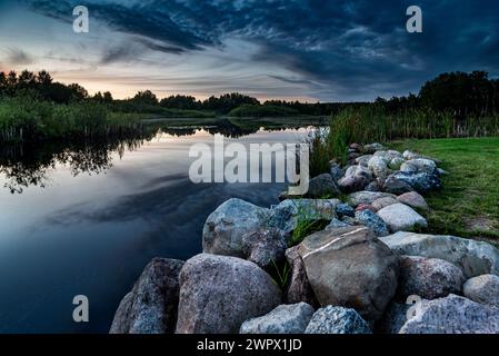 Paysage pittoresque vue de beau coucher de soleil sur le lac pittoresque avec le ciel et les nuages reflétés sur l'eau avec des rochers et des pierres au premier plan. Banque D'Images