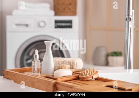 Plateau de bain en bois avec différentes fournitures et produits cosmétiques dans la salle de bains lumineuse Banque D'Images