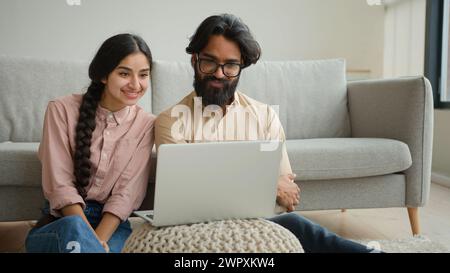 Couple multiracial homme arabe et femme indienne sur le plancher famille couple propriétaires femme petite amie et mari petit ami regardant le film portable Smart TV Banque D'Images