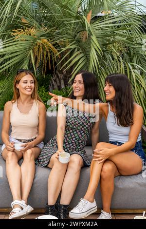 Trois femmes assises sur un canapé, une pointant vers quelque chose. Ils sourient tous et tiennent des tasses. Banque D'Images