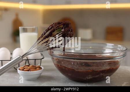 Fouetter avec la crème au chocolat, bol et différents produits sur la table en marbre gris dans la cuisine Banque D'Images