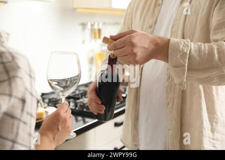 Homme ouvrant bouteille de vin avec tire-bouchon tandis que femme tenant verre à vin à l'intérieur, gros plan Banque D'Images