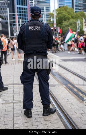 Un policier tatoué surveille les manifestants lors d'une marche à Sydney pour soutenir les Palestiniens dans la guerre de Gaza. Banque D'Images