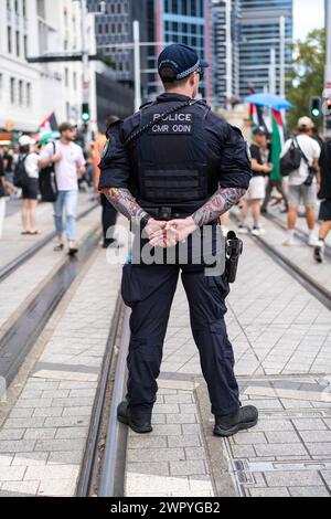 Un policier tatoué surveille les manifestants lors d'une marche à Sydney pour soutenir les Palestiniens dans la guerre de Gaza. Banque D'Images