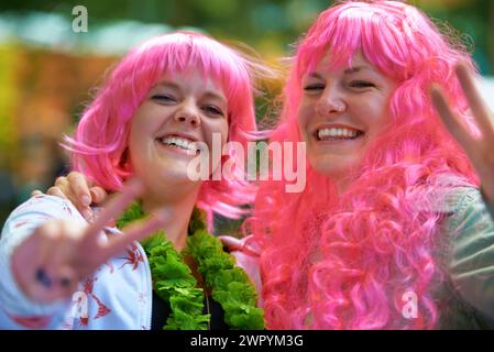 Portrait, festival de musique et femmes en perruques, amis et signe de paix avec plaisir et bonheur. Visage, les gens et les filles avec costume et habiller avec joie Banque D'Images