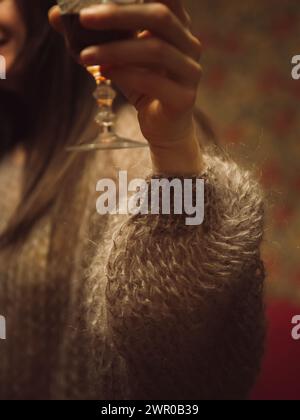 Gros plan vertical de la main d’une femme dans un délicat pull maille violette tenant un verre de vin. Banque D'Images