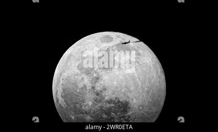 la lune se lève contre un ciel noir profond et un avion passe avec une traînée de condensation Banque D'Images