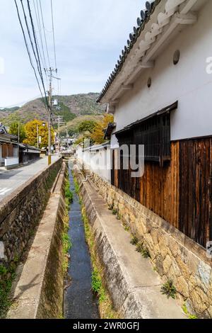 Route étroite avec un fossé de drainage le long de celle-ci, et murs en bois et en plâtre blanc des bâtiments dans la vieille ville de château de Tatsuno au Japon. Banque D'Images