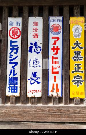 Quatre enseignes métalliques étroites rouillées vintage faisant la publicité de différentes marques de bière japonaise clouées sur un cadre de fenêtre en bois à lattes à Tatsuno, au Japon. Banque D'Images