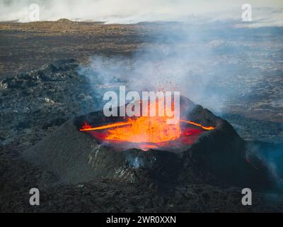 Éruption volcanique en Islande, cratère sommital, expulsion de gaz, et lave fondue se déversant d'un évent, vue latérale aérienne. Risques naturels et géothermie e Banque D'Images