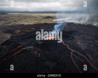 Vue panoramique spectaculaire d'une éruption volcanique active en Islande, une fissure volcanique libérant un flux de lave se jetant dans une vallée, plan large aérien. Banque D'Images