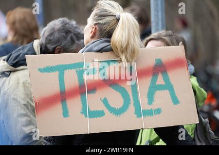 10 mars 2024, Brandebourg, Grünheide : lors d'une manifestation contre l'expansion de Tesla sous le slogan 'Tesla No Thanks!', un participant porte une pancarte avec le mot 'Tesla' barré. Photo : Christophe Gateau/dpa Banque D'Images